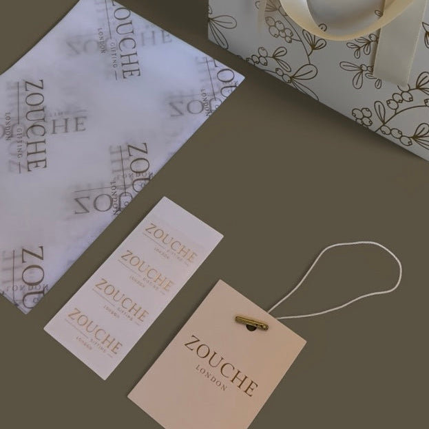 Zouche London packaging including a gift bag, tags, and a ribbon on a dark background.