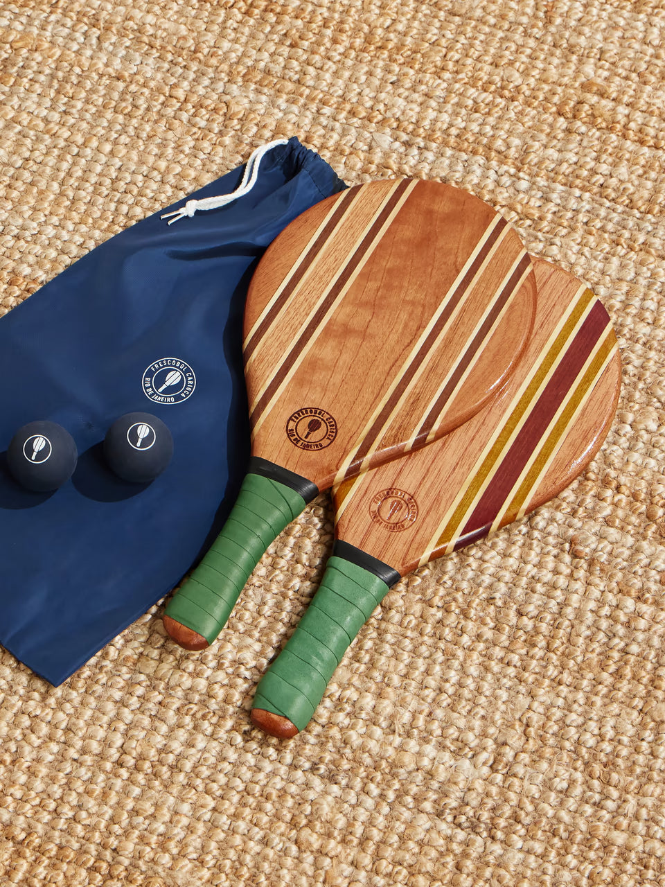 Wooden pickleball paddle with green handles, blue pouch, and two black balls on a textured surface