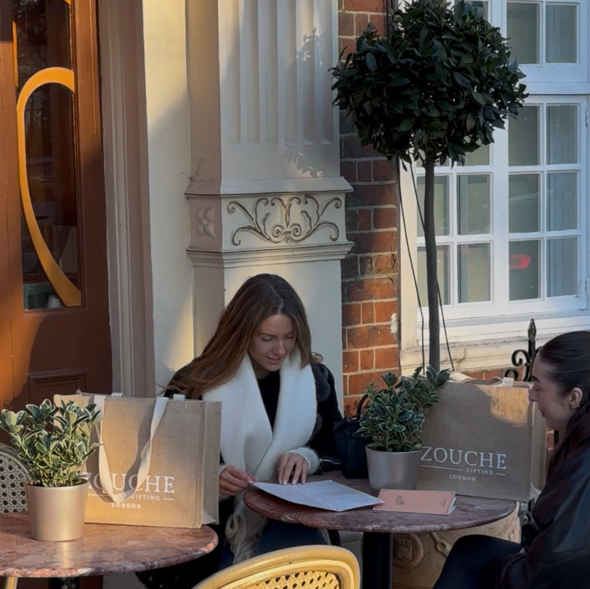 Two women sitting at a table with Zouche products in an outdoor setting.