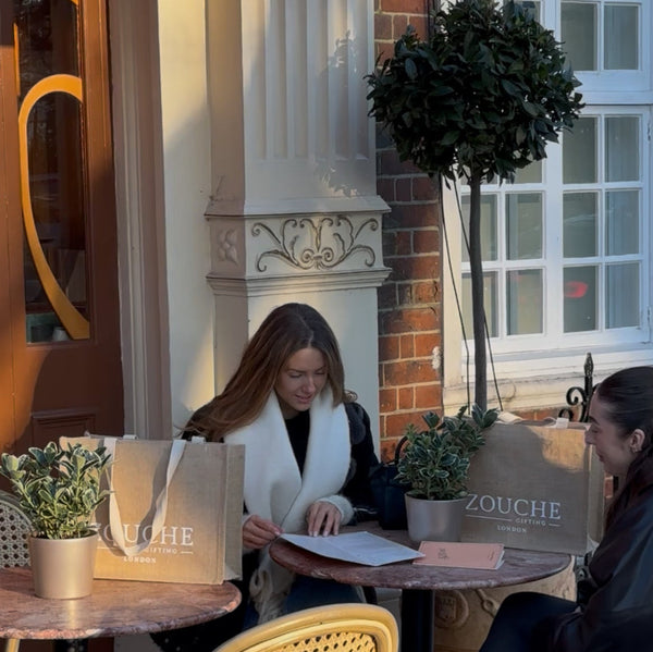 Two women sitting at a table with Zouche products in an outdoor setting.